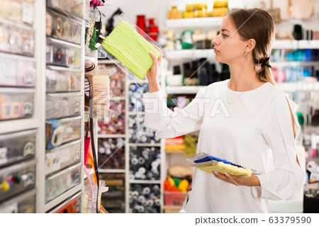 Interested young woman choosing colorful ribbons and braid for dressmaking in sewing supplies shop Interested young woman choosing colorful ribbons and braid for dressmaking in sewing supplies shop 63379590
