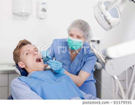 Male patient sitting on chair in dental office getting dentist treatment Male patient sitting on chair in dental office getting dentist treatment 63379591