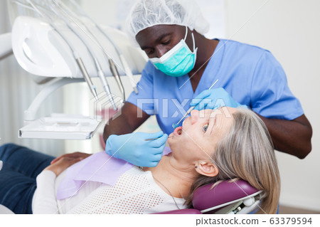 Dentist is treating female patient which is sitting in dental chair in clinic Dentist is treating female patient which is sitting in dental chair in clinic 63379594