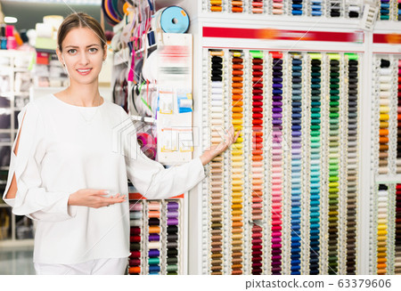 Young female seller of sewing supplies shop showing colored threads for dressmaking Young female seller of sewing supplies shop showing colored threads for dressmaking 63379606