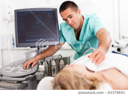 Young man sonographer using ultrasonography machine checking female patient in hospital diagnostic room 63379691