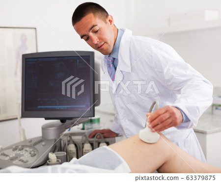 Man doctor during ultrasound test of young woman of knee Man doctor during ultrasound test of young woman of knee 63379875