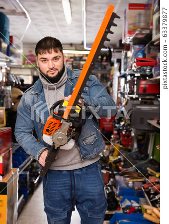 Adult male is standing with new electric brush cutter in tools store Adult male is standing with new electric brush cutter in tools store 63379877
