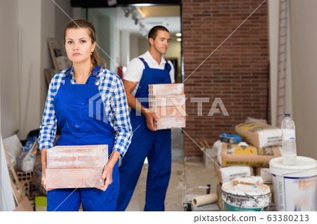 Man and woman in work overalls carrying bricks during finishing work in room of public space Man and woman in work overalls carrying bricks during finishing work in room of public space 63380213