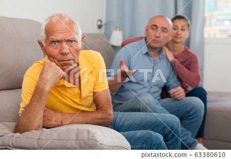 Upset senior man sitting at home on comfortable sofa, adult children 63380610