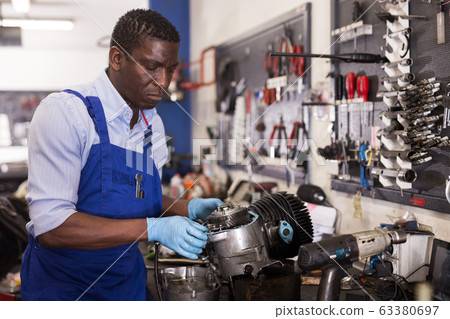 Afro american worker in overalls inspects a motorcycle engine 63380697