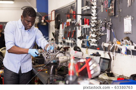 Afro american worker repairing a motorcycle engine in a garage Afro american worker repairing a motorcycle engine in a garage 63380763