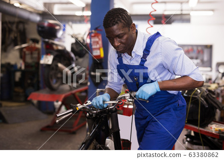 Service engineer repairing motorcycle in motorcycle service Service engineer repairing motorcycle in motorcycle service 63380862