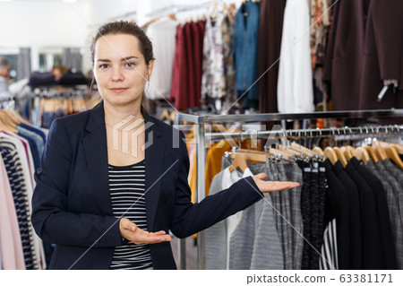 Portrait of shop assistant standing among clothes Portrait of shop assistant standing among clothes 63381171