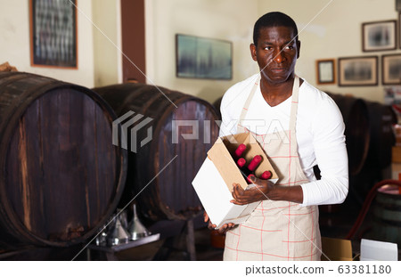 Positive afro seller working in wine store, holding box full of bottles with wine Positive afro seller working in wine store, holding box full of bottles with wine 63381180