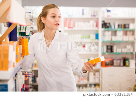 Portrait of diligent smiling pleasant positive female druggist in white coat working in pharmacy Portrait of diligent smiling pleasant positive female druggist in white coat working in pharmacy 63381194