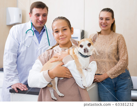 Cheerful mother and daughter visiting veterinarian clinic with their puppy Cheerful mother and daughter visiting veterinarian clinic with their puppy 63381232