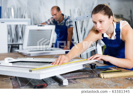 Female worker measuring finished metal-plastic window in workshop 63381345