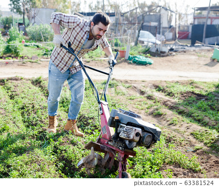 Man professional gardener using plow at land with green grass in garden Man professional gardener using plow at land with green grass in garden 63381524