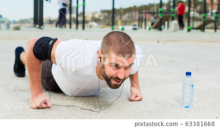 man performs push-ups on sportsground 63381668