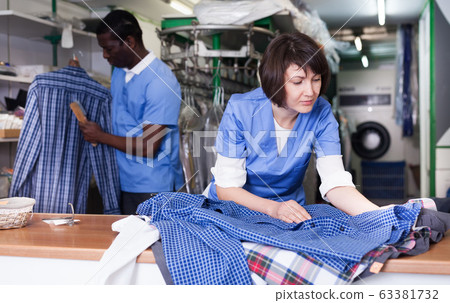 Female laundry worker examining clean garments Female laundry worker examining clean garments 63381732