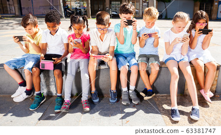 Children using mobile devices outdoors at sunny day Children using mobile devices outdoors at sunny day 63381747