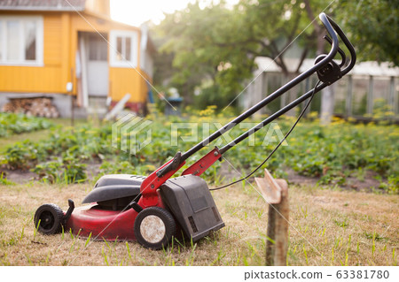 Grass mower stands on green lawn in summer garden Grass mower stands on green lawn in summer garden 63381780