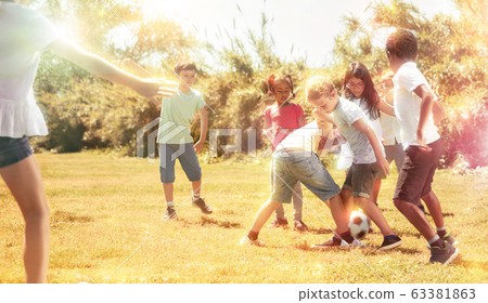 Cheerful children are jogning with ball on the playground. 63381863