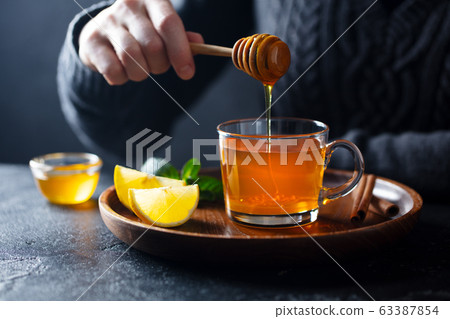 Cup of tea with pouring honey and lemon. Grey background. Cup of tea with pouring honey and lemon. Grey background. 63387854