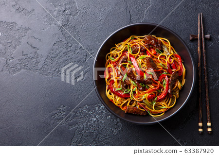 Stir fry noodles with vegetables and beef in black bowl. Slate background. Copy space. Top view. 63387920