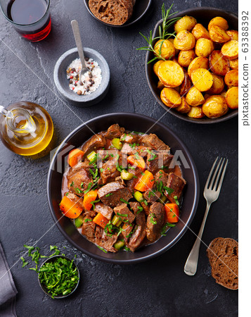 Beef meat and vegetables stew in black bowl with roasted baby potatoes. Dark background. Top view. Beef meat and vegetables stew in black bowl with roasted baby potatoes. Dark background. Top view. 63388392