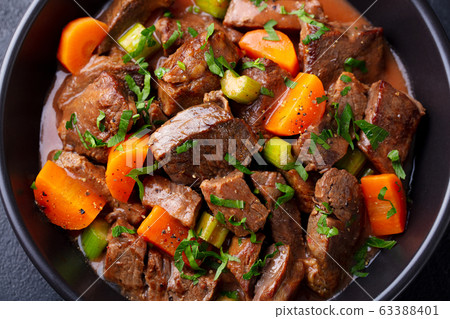 Beef meat and vegetables stew in black bowl. Dark background. Close up. 63388401