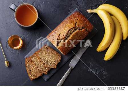 Banana, coconut bread, cake with cup of tea on slate board. Dark stone background. Copy space. Top view. 63388887
