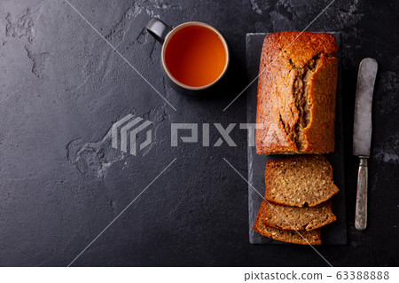 Banana, coconut bread, cake with cup of tea on slate board. Dark stone background. Copy space. Top view. 63388888