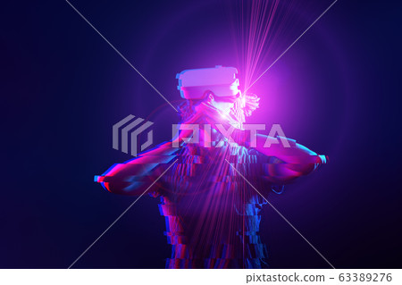 Woman is using virtual reality headset. Neon light studio portrait. Image with glitch effect. 63389276
