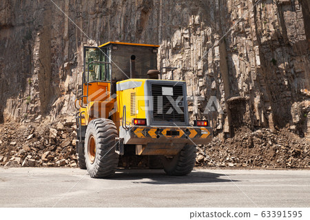 Yellow tractor clears a mountain road from rocks Yellow tractor clears a mountain road from rocks 63391595