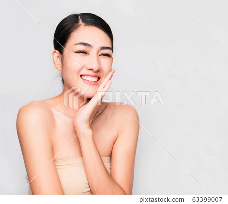 young beautiful asian woman with clean and bright skin, Cosmetic Beauty Concept,hands touch on the cheek, smiling and friendly face isolated on grey background 63399007
