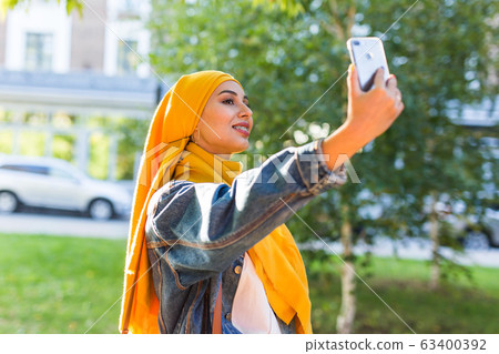 Muslim girl in hijab makes a selfie on the phone standing on the street of the city 63400392