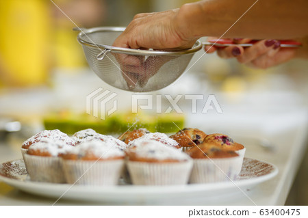 Confectioner sprinkles freshly baked muffins with 63400475