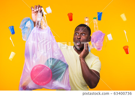 Problem of trash, plastic recycling, pollution and environmental concept - surprised man carrying garbage bag on yellow background 63400736