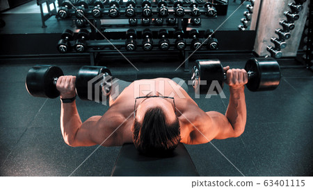 A man bodybuilder in glasses pumping his hands muscles lying on the stand in the gym A man bodybuilder in glasses pumping his hands muscles lying on the stand in the gym 63401115
