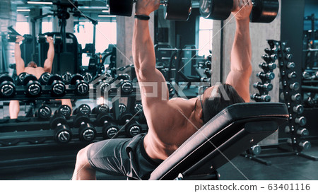 A man bodybuilder pumping his hands muscles lying on the stand in the gym 63401116