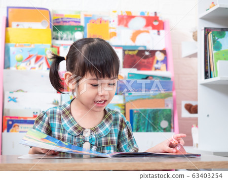 Asian little cute girl sitting and reading the tale book on table. Preschool lovely kid reading the book. Learning and education of kid. Asian little cute girl sitting and reading the tale book on table. Preschool lovely kid reading the book. Learning and education of kid. 63403254