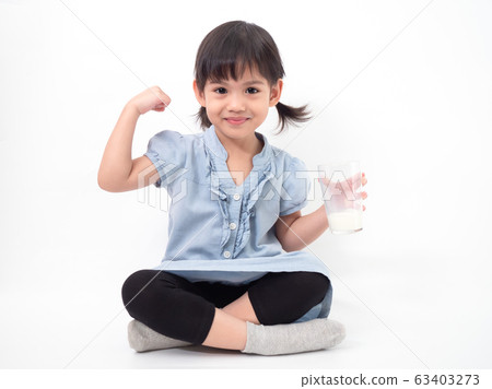 Asian little cute girl 4 years old holding and drinking milk from glasses and raising her arm to be strong on white background. Milks is essential and nutrition for the child's body. 63403273