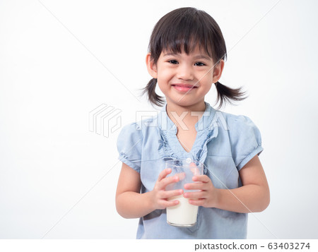 Asian little cute girl 4 years old holding and drinking milk from glasses over white background. Milks is essential and nutrition for the child's body. Asian little cute girl 4 years old holding and drinking milk from glasses over white background. Milks is essential and nutrition for the child's body. 63403274
