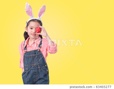 Happy little cute girl 6 years old wearing rabbit ears and holding red easter eggs close her eye on yellow background with clipping part. Happy little cute girl 6 years old wearing rabbit ears and holding red easter eggs close her eye on yellow background with clipping part. 63403277