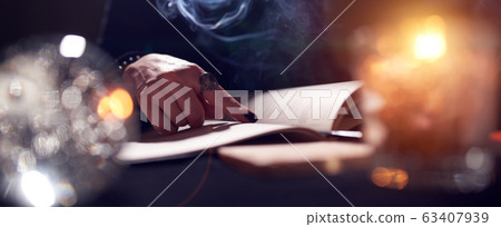 Close-up of fortune-teller's hands, book of predictions, burning candle 63407939