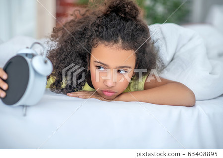 Awakened girl with brown eyes looking at the alarm clock. Awakened girl with brown eyes looking at the alarm clock. 63408895