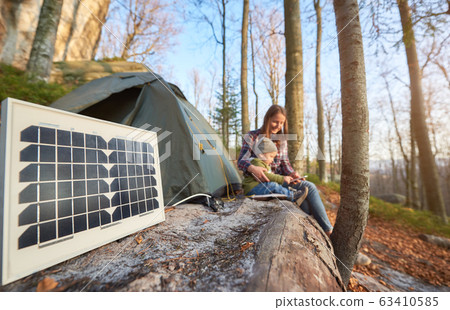 Close up solar battery in campsite on sunny autumn day against the background of young family Close up solar battery in campsite on sunny autumn day against the background of young family 63410585
