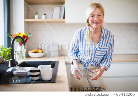 Portrait of senior woman washing dishes indoors at home. Portrait of senior woman washing dishes indoors at home. 63418200
