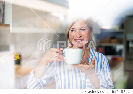 Portrait of senior woman with cup of coffee indoors at home. Portrait of senior woman with cup of coffee indoors at home. 63418202