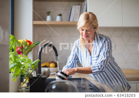 Portrait of senior woman washing dishes indoors at home. Portrait of senior woman washing dishes indoors at home. 63418203