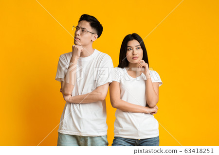Thoughtful asian couple posing over yellow background 63418251