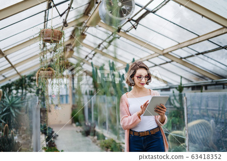 Woman researcher standing in greenhouse, using tablet. Woman researcher standing in greenhouse, using tablet. 63418352
