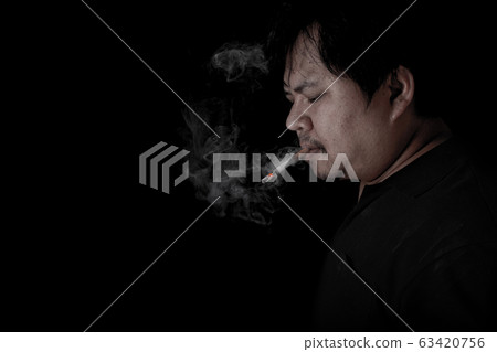 The fat man lighting up a joint with lighter smoking at the black background 63420756